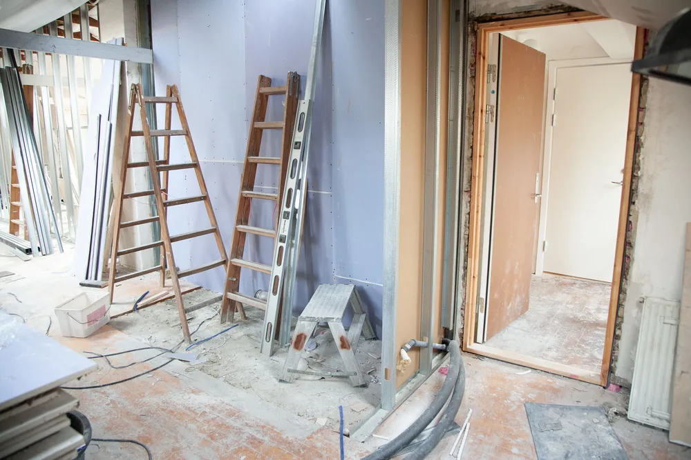 Interior under renovation with ladders, exposed framing and construction debris
